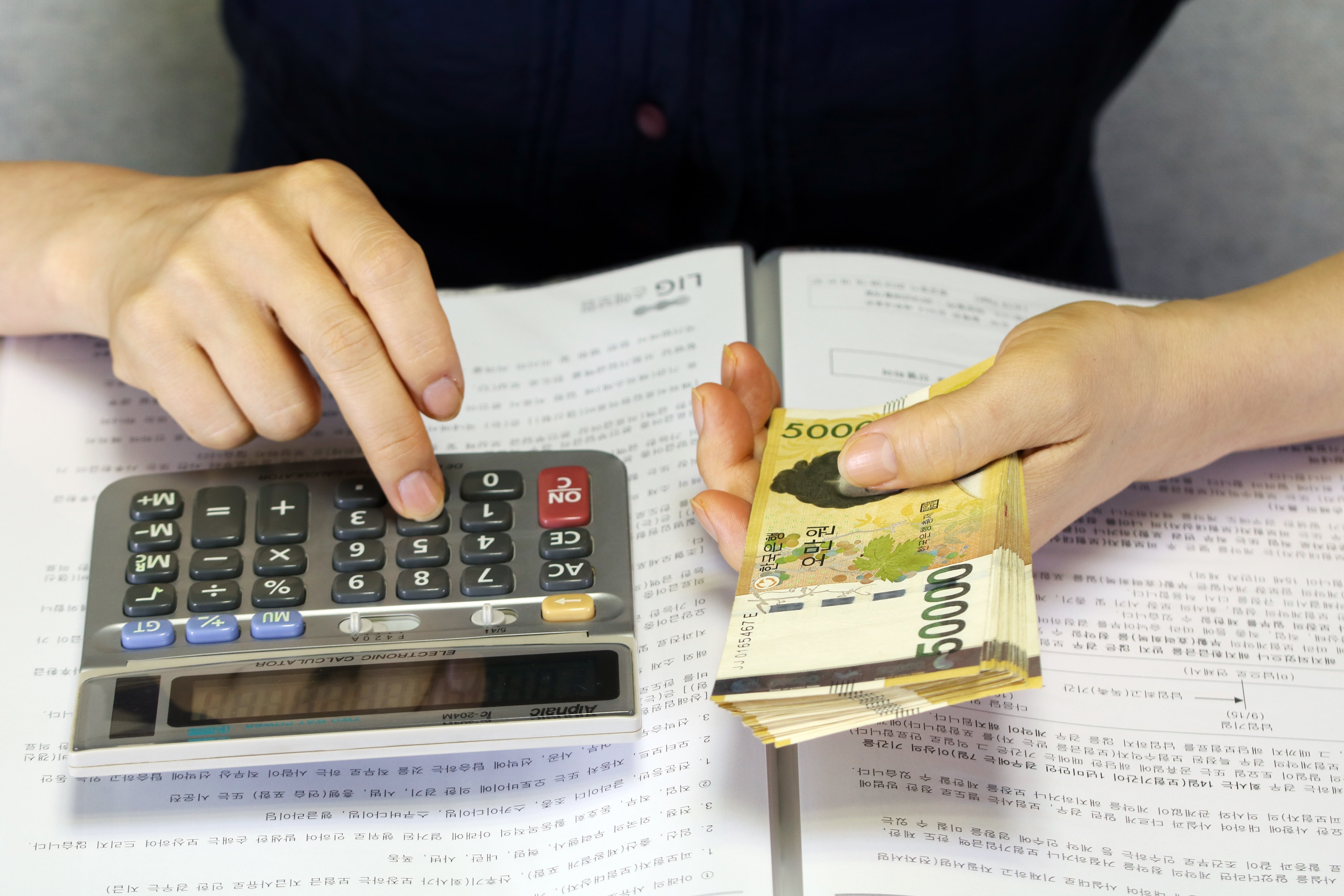 계산기를 두드리며 통장 옆에서 현금을 세는 손