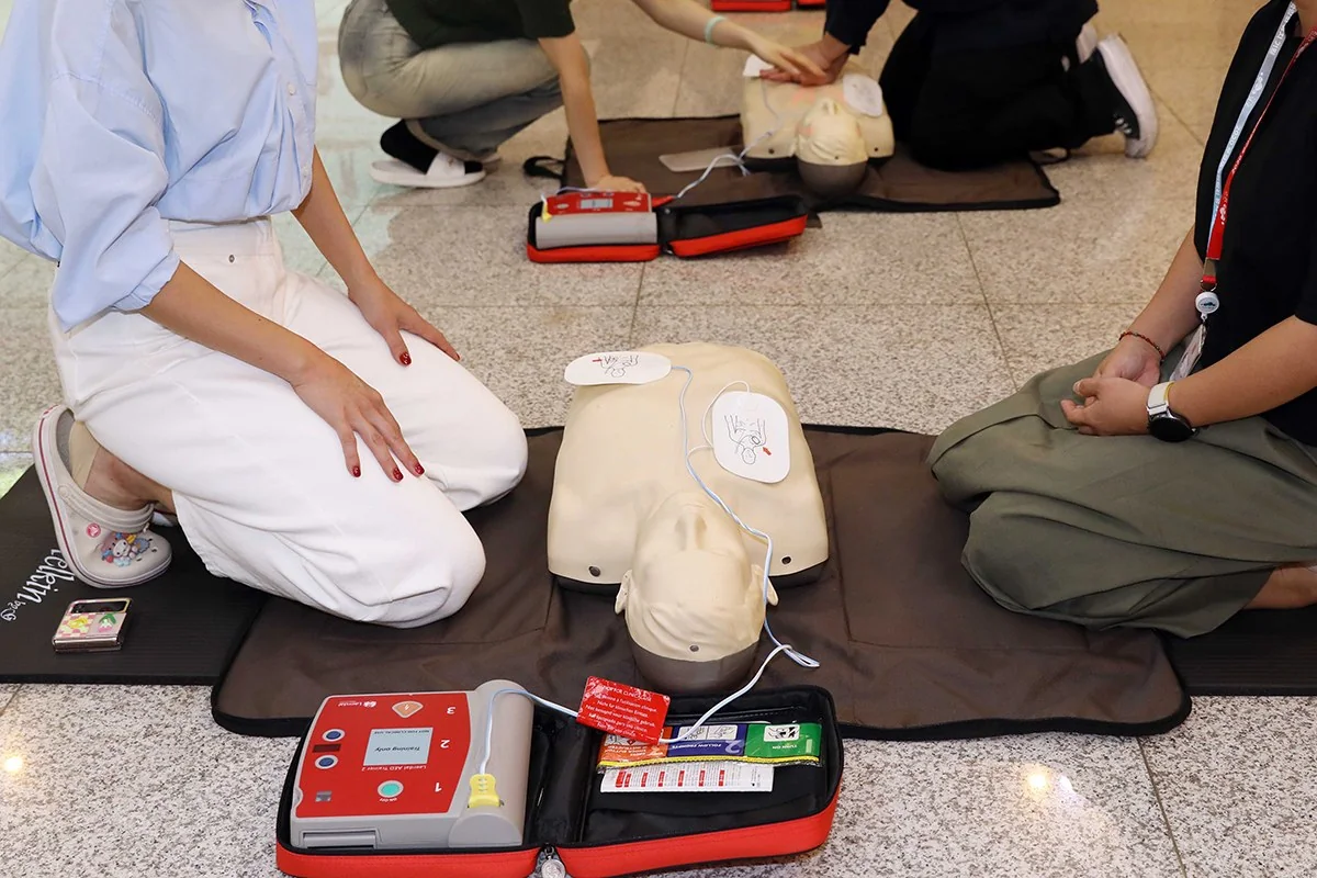 사람 얼굴 없이 AED 본체와 연결선, 마네킹에 붙인 패드를 보여주는 교육 장면
